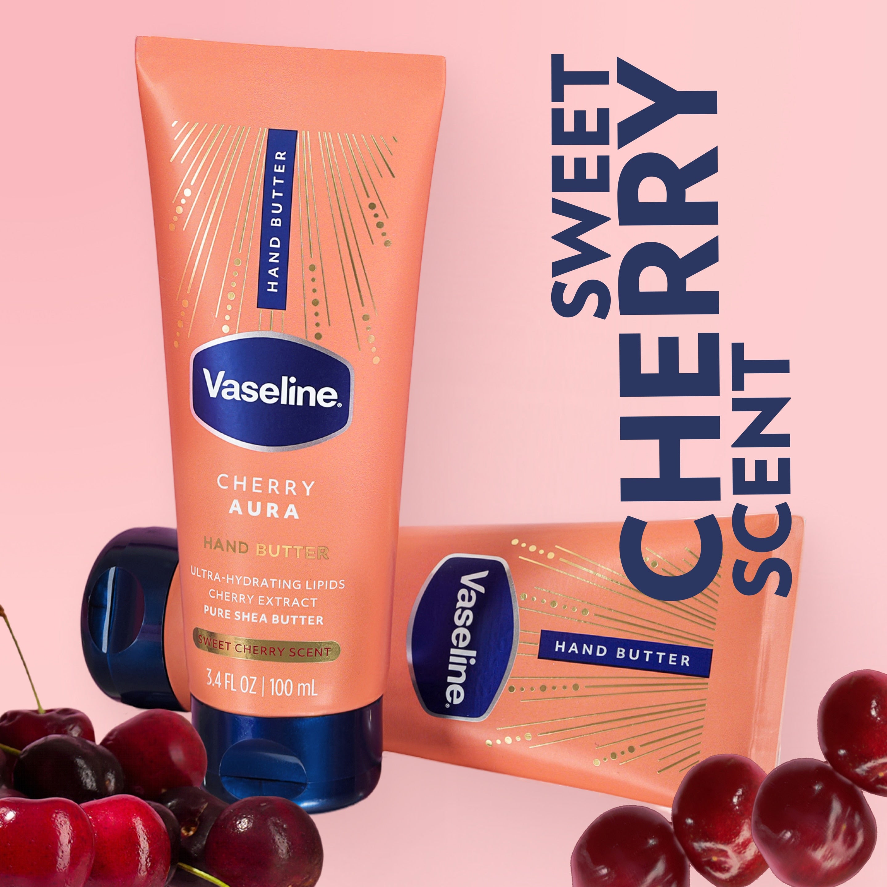 Two tubes of Vaseline Cherry Aura Hand Butter are displayed with fresh cherries on a pink background with text